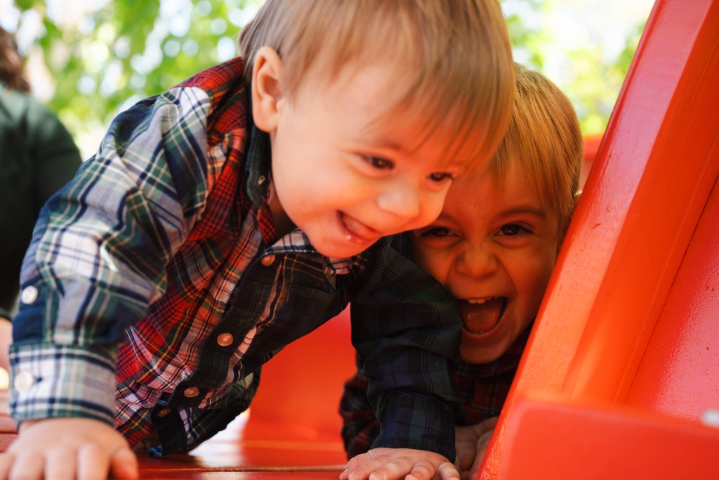 Two young brothers laughing on a playground slide